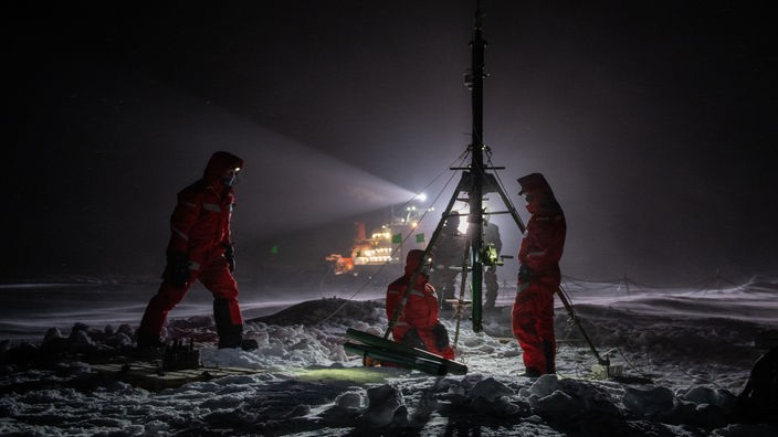 Wissenschaftler stehen im Dunkeln auf der Eisscholle vor der Polarstern bei einem Messgerät.