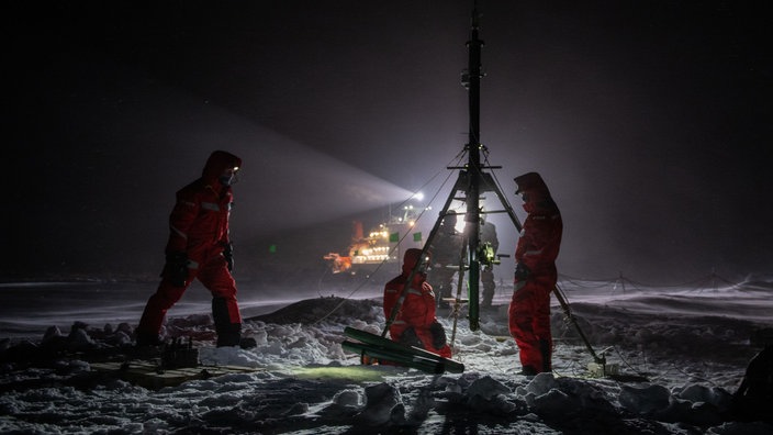 Wissenschaftler stehen im Dunkeln auf der Eisscholle vor der Polarstern bei einem Messgerät. | Bildquelle: Alfred-Wegener-Institut, E. Horvath Wissenschaftler stehen im Dunkeln auf der Eisscholle vor der Polarstern bei einem Messgerät.