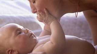 Ein nackter Säugling betastet das Gesicht seiner Mutter.