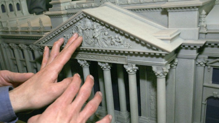 Hände betasten den Eingangsbereich eines Modells vom Reichstag.