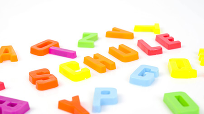 Plastik-Buchstaben in verschiedenen Farben auf weißem Hintergrund.
