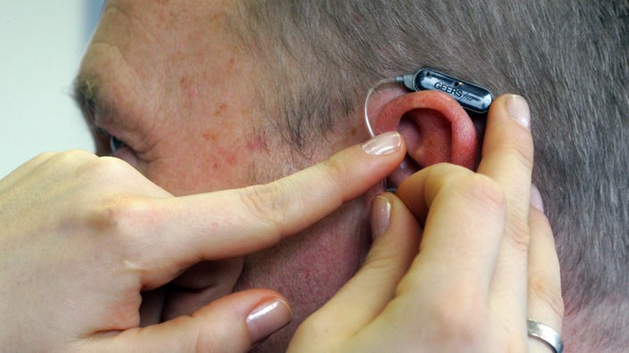 Eine Hörgerät wird am Ohr eines Mannes befestigt.