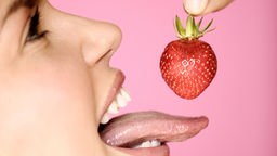 Eine Frau isst mit weit herausgestreckter Zunge eine Erdbeere.
