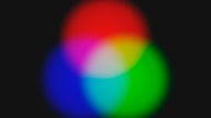 Additive Farbmischung: Die Projektion von orange-rot, grün und violettblauen Lichtkreisen ergibt in der Überschneidung die drei Primärfarben Zyan, Magenta, Gelb – und in der Mitte weißes Licht.