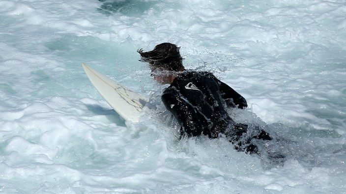 Surfer paddelt auf Brett in eine Welle
