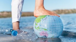 Der Fuß eines Menschen ruht auf einem aufblasbaren Wasserball, der aussieht wie die Erde