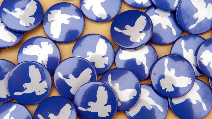 Auf blauen Buttons zum Anstecken prangt die weiße Friedenstaube. | Bildquelle: dpa Auf blauen Buttons zum Anstecken prangt die weiße Friedenstaube.