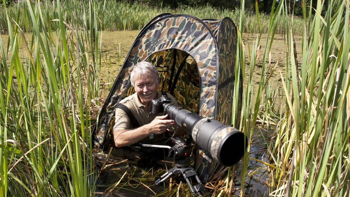 Fotograf Sebastian Körner mit seiner Kamera in einem Tarnzelt zwischen hohen Gräsern