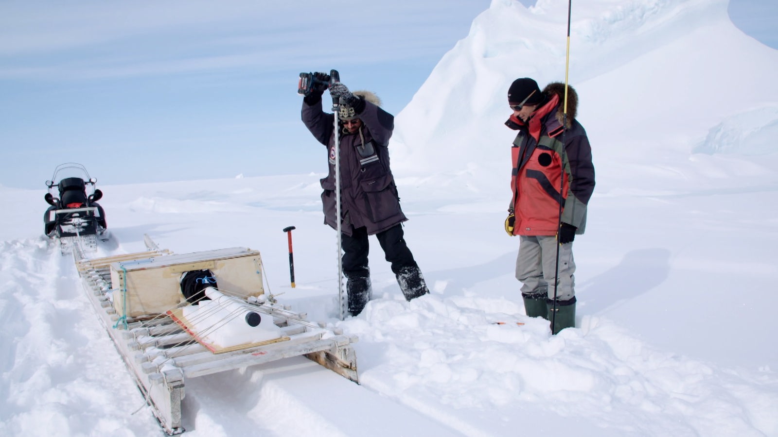 Zwei Männer bohren im Schnee in der Arktis.