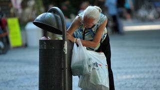 Eine ältere Frau wühlt in einem Mülleimer