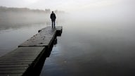 Ein Mann steht einsam am Ende eines Bootsstegs und schaut auf den Nebel am See.
