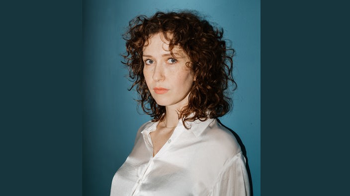 Porträtaufnahme von Katja Lewina vor petrolfarbenem Hintergrund.