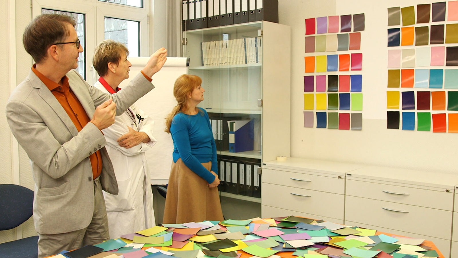 Eine Ärztin und zwei andere Personen diskutieren über Farbproben an der Wand