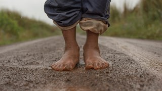 Zwei nackte Füße stehen auf einer matschigen nassen Straße 