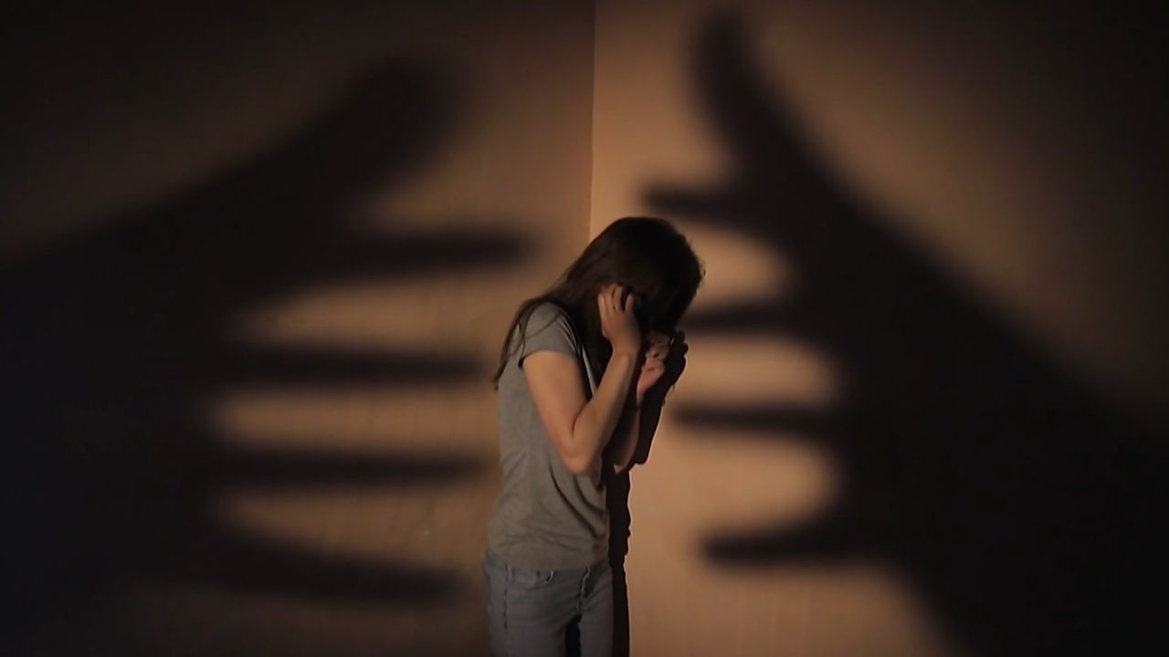 Eine Frau steht in einer Ecke, zwei riesige Schattenhände greifen nach ihr