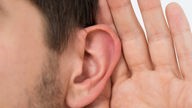 Ein Mann hält sich die Hand an sein Ohr, um besser hören zu können.