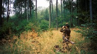 Jäger mit Jagdhund im Wald und schaut durch ein Fernglas