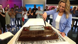 Planet-Wissen-Moderatorin Andrea Grießmann schneidet eine Torte an, dahinter stehen viele Menschen und applaudieren