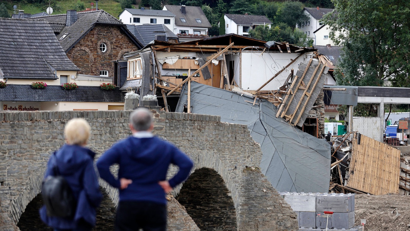 Zwei Menschen von hinten, die die Zerstörung im Ahrtal nach der "Jahrhundertflut" 2021 betrachten 