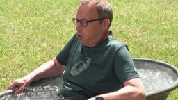 Ein Mann im grünen T-Shirt sitzt in einer Zinkwanne mit Eiswasser.