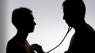 Schemenhafte Darstellung: Ein Arzt untersucht einen männlichen Patienten mit dem Stethoskop