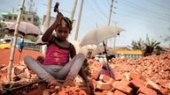 Ein Mädchen zerkleinert mit einem Hammer Ziegelsteine in Bangladesh