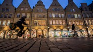 Zwei Fahrradfahrer vor der abendlich beleuchteten Kulisse des Prinzipalmarkts in Münster 