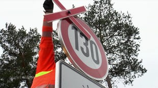 An einem Verkehrsschild (130 Geschwindigkeitsbeschränkung) wird ein rotes Kreuz für dessen Aufhebung wieder abgenommen.
