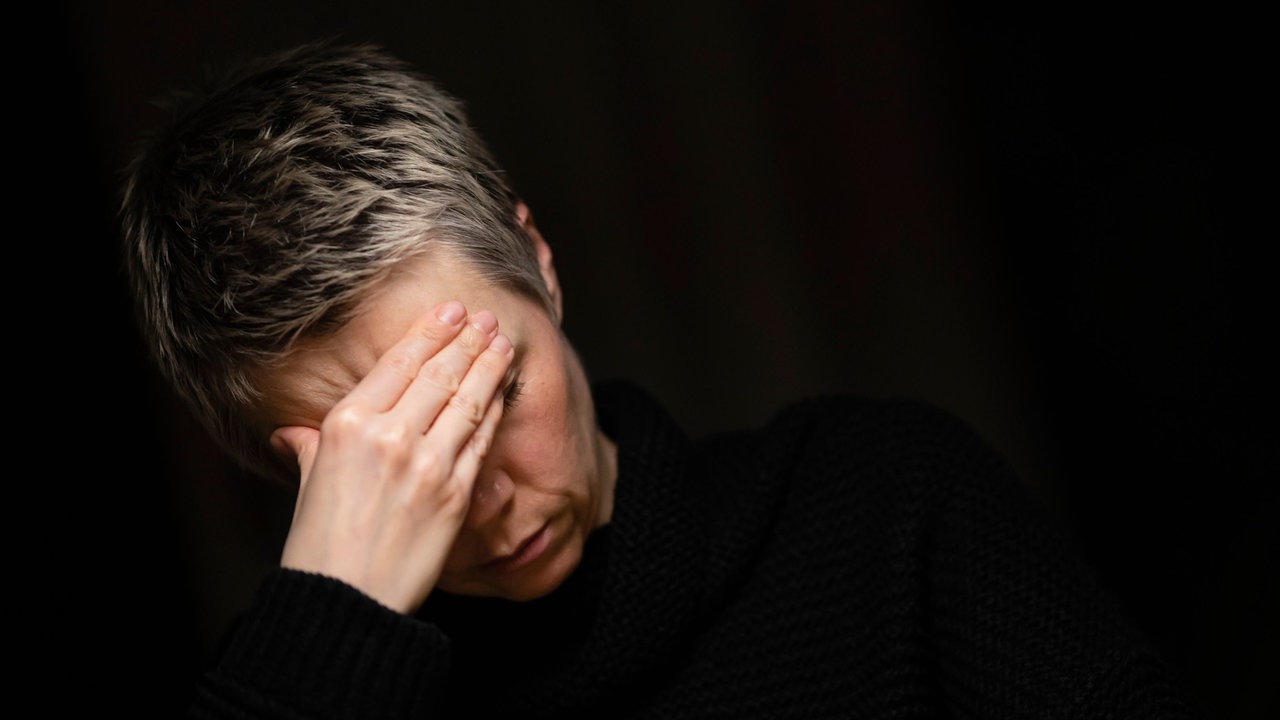 Eine Frau sitzt allein am Tisch und hält sich die Hände vor das Gesicht