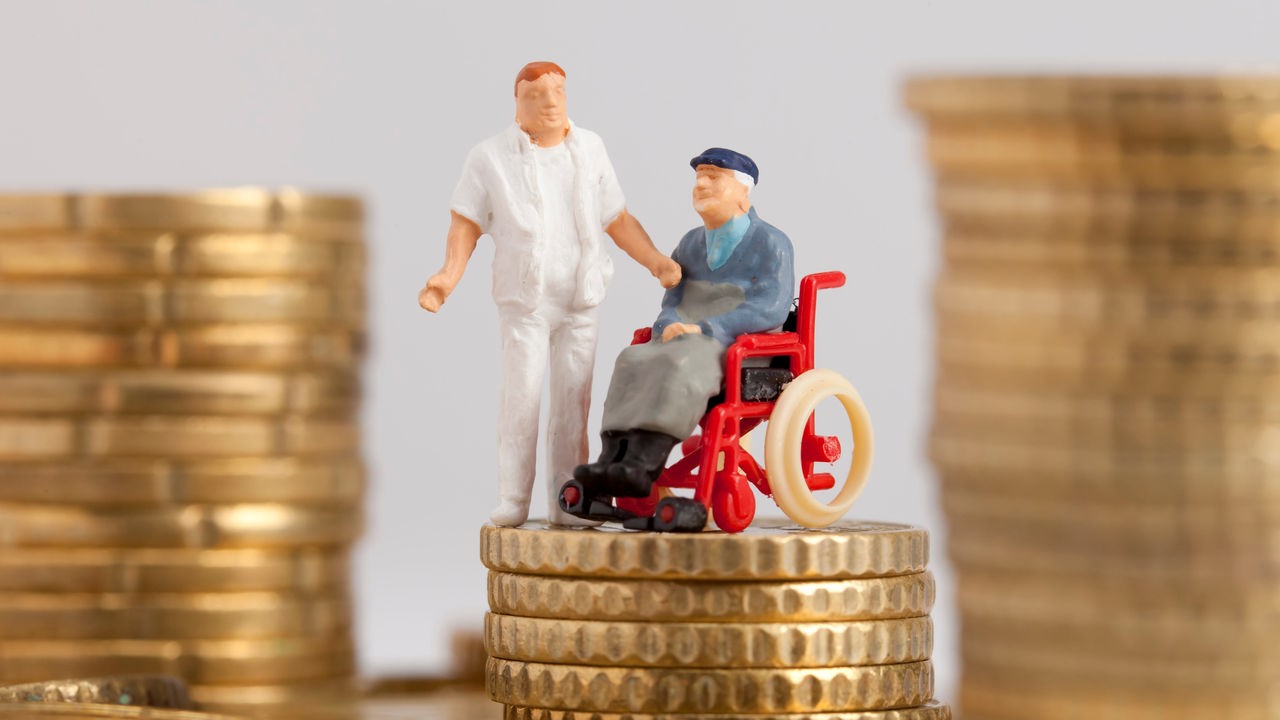 Figur im Rollstuhl und Figur eines Pflegers auf Geldmünzen