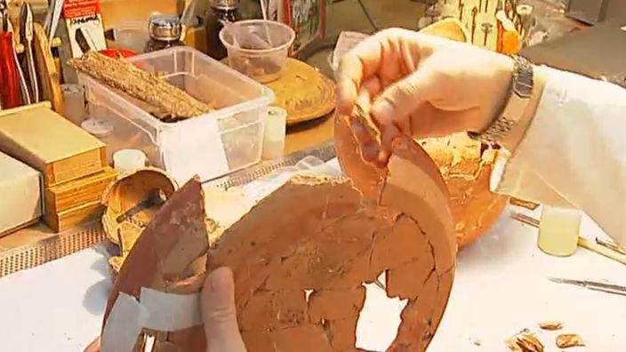 Eine Archäologin setzt Stücke eines Tellers zusammen.