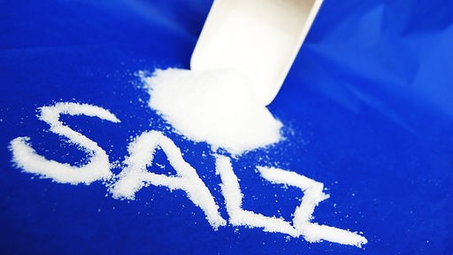 Salz vor einem umgekippten Behälter, davor steht mit Salzkrümeln das Wort "Salz" geschrieben 