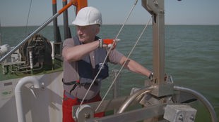 Ein Mann steht auf einem Forschungsschiff und zeigt aufs Meer