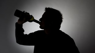 Silhouette eines Mannes, der aus einer Flasche Wein trinkt