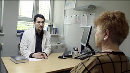 Arzt und Alzheimer-Patientin am Schreibtisch