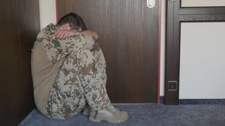 Ein Soldat in Tarnkleidung hockt in einer Ecke und verbirgt den Kopf unter den Armen