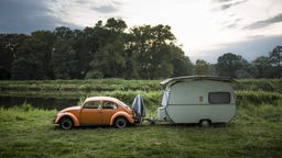 Ein VW Käfer steht mit einem Wohnwagen am Elbufer bei Havelberg