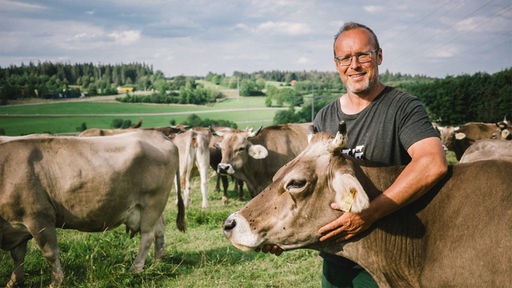 Ein Biolandwirt steht auf der Weide und hat seinen Arm um den Hals einer Kuh gelegt.
