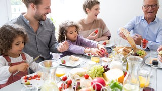 Vater, Mutter, zwei Kinder und Großvater sitzen an einem Tisch und frühstücken