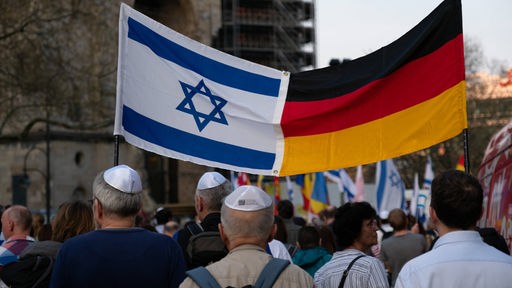Menschen auf einer Demonstration. Viele tragen eine Kippa. Man sieht eine deutsche neben einer israelischen Flagge