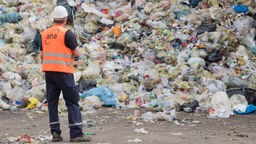 Ein Mann mit Warnweste blickt auf einen Berg Plastikmüll auf einer Deponie in Hannover