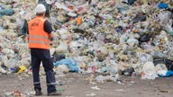 Ein Mann mit Warnweste blickt auf einen Berg Plastikmüll auf einer Deponie in Hannover