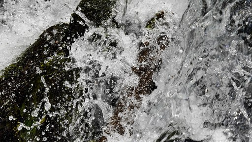 Klares Quellwasser fließt spritzend über Steine.