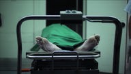 Die bloßen Füße eines mit einem grünen Tuch bedeckten Leichnams auf einer Edelstahlbahre.