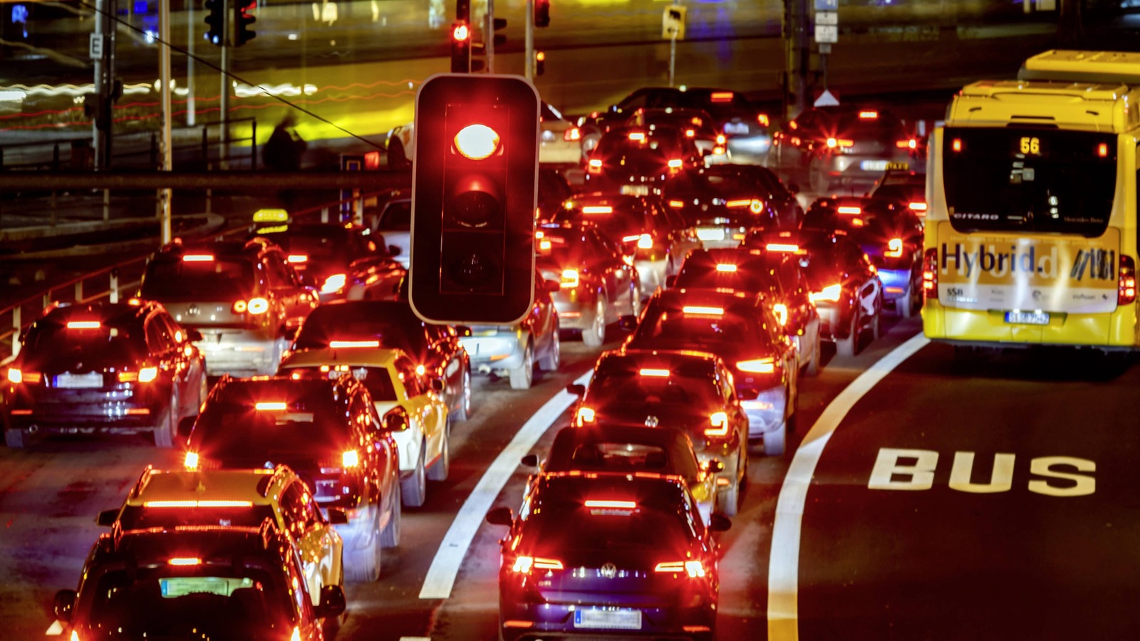 Nächtliche Autoschlange in der Stadt mit einer roten Ampel im Vordergrund.