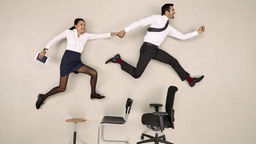 Frau und Mann in Bürokleidung springen Hand in Hand über Stühle.