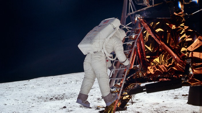 Ein Astronaut im Anzug klettert auf einer Leiter von seiner Raumkaspel auf die Mondoberfläche.