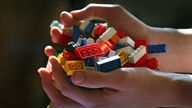 Zwei Kinderhände halten Legosteine.