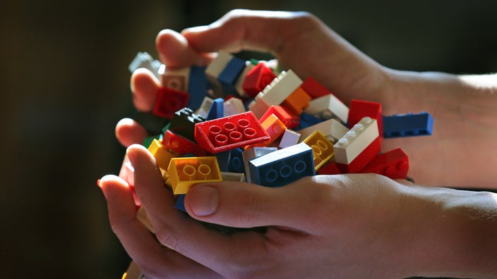 Zwei Kinderhände halten Legosteine.