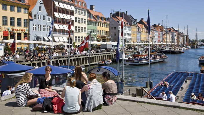 Junge Touristen sitzen entspannt am Nyhavn-Kanal in Kopenhagen.